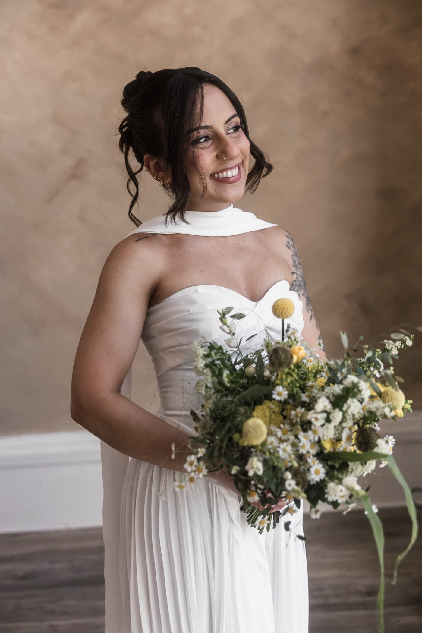Bride smiling straight at the camera, holding a wildflower bouquet.