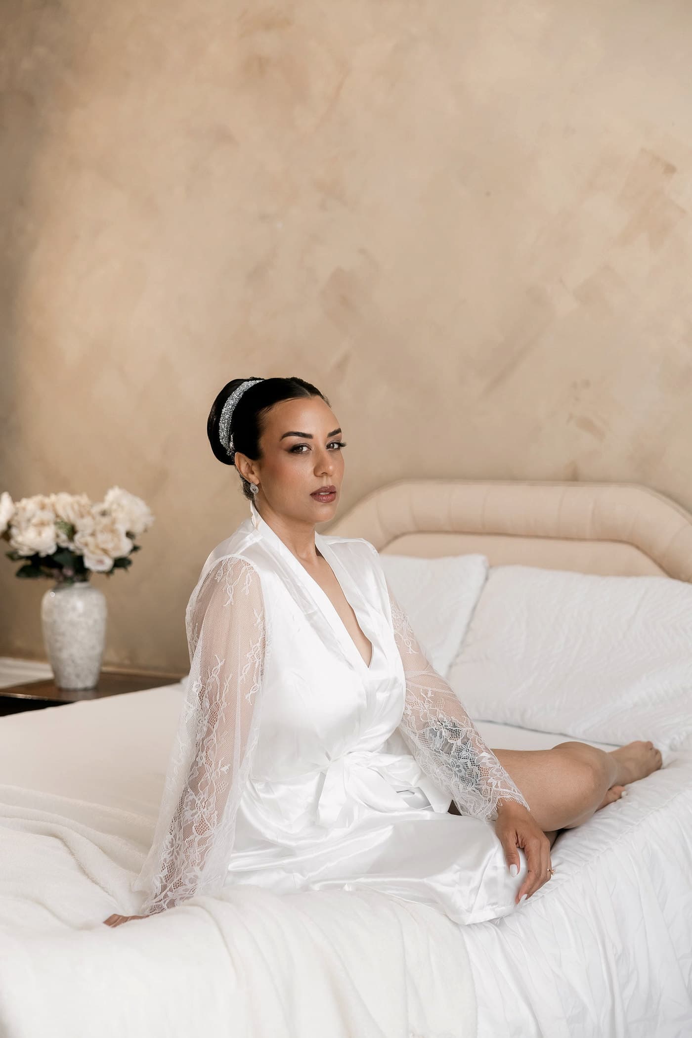 Bride in a lace robe sitting on a bed on the morning of her wedding.