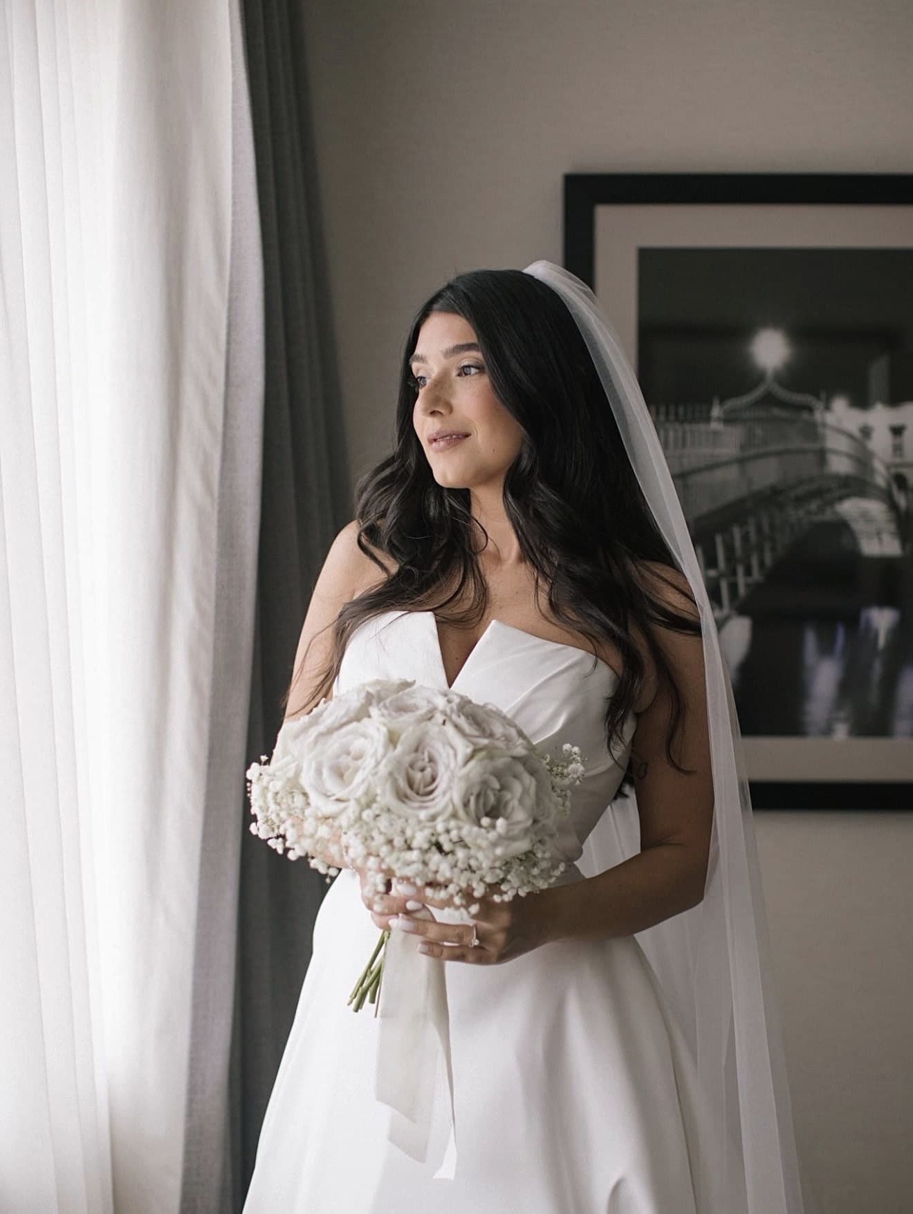 Bride in profile under a long veil, holding a white bouquet.