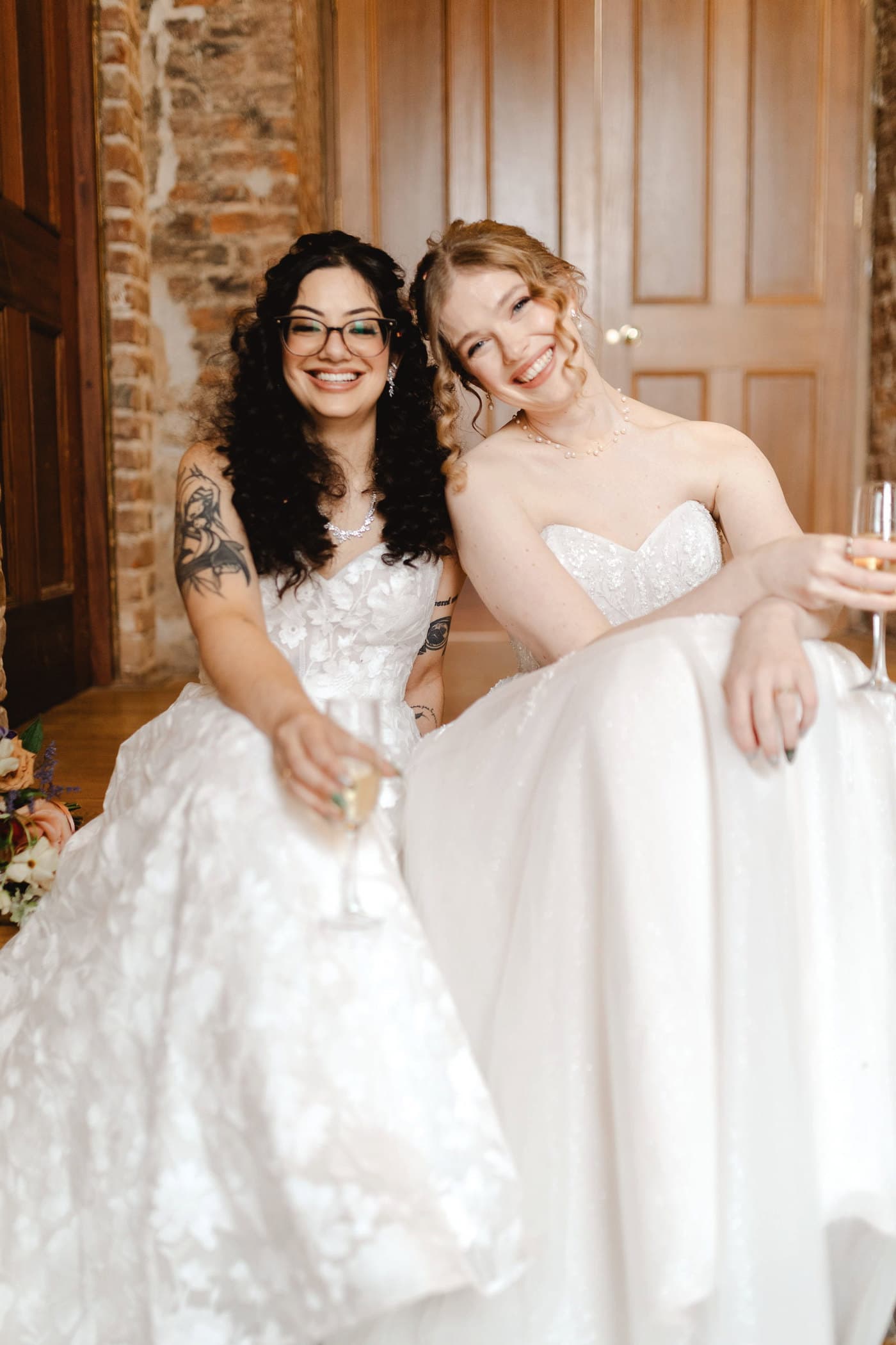 Two brides raising their glasses to each other.
